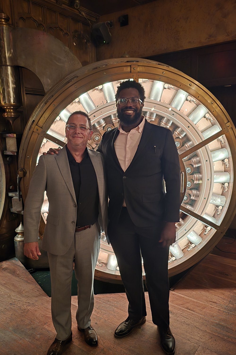 Otuoze Baiye and Javier L&oacute;pez Ramos standing in front of the vault
                    door at The Vault at Trinity Place.